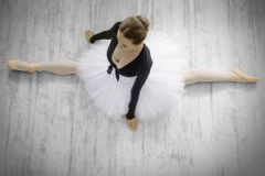 Classical Ballet dancer portrait. Beautiful graceful ballerine in tutu skirt practice split ballet position in class room background. Ballet class training, high-key soft toning. Top view from above
